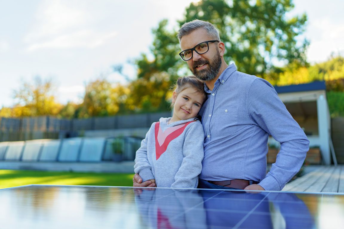 father and daughter smiling in backyard behind a solar panel