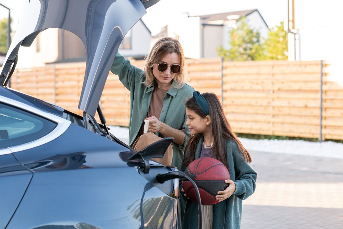 mother and her daughter standing by trunk of a charging Tesla in their driveway