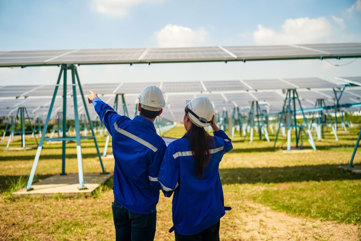 two workers with hardhats looking out on a field of solar panels