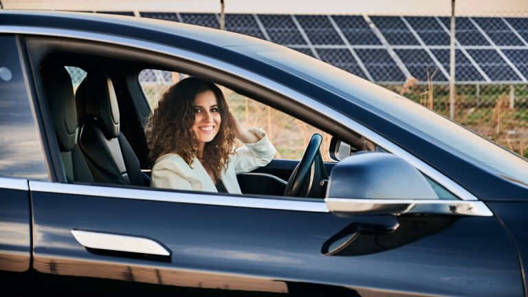 woman driving electric vehicle in front of solar panels